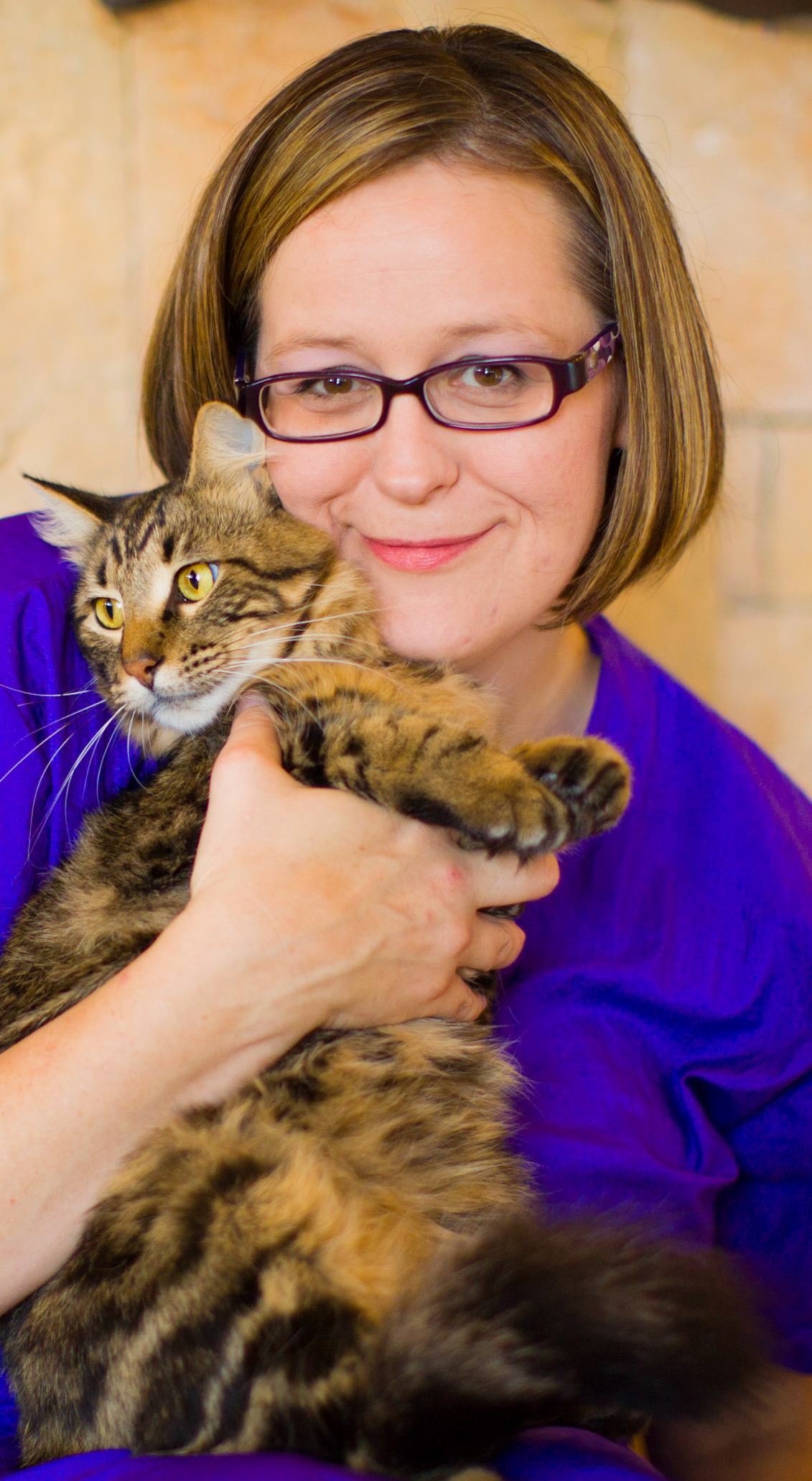 Aunt Stacey smiles facing the camera while holding a brown tabby cat up next to her face and chest